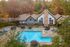 Charming outdoor pool area featuring a cozy house with a stone chimney, surrounded by colorful autumn trees and inviting lounge chairs.