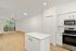 Bright modern apartment interior featuring an open-concept kitchen with sleek white cabinets and stainless steel appliances, leading into a spacious living area with natural light through large patio doors.