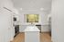 Bright and modern kitchen with sleek white cabinetry, stainless steel appliances, and a large window offering a scenic view of lush greenery.
