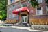 Charming brick apartment building entrance with a vibrant red canopy and elegant front steps, set amidst lush landscaping.