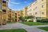 Welcoming apartment complex courtyard with vibrant greenery and modern architecture under a clear blue sky.
