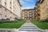 Charming apartment complex with classic architecture, featuring lush green landscaping and a welcoming entrance pathway under a vibrant blue sky.