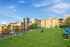 Vibrant outdoor communal garden with lush green grass and playful seating areas, set against the backdrop of charming historic buildings and modern skyscrapers.