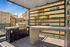 Chic rooftop terrace with a modern grill and spacious dining area, perfect for entertaining against a sunny urban backdrop.