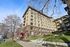 Charming vintage apartment building with classic architecture, nestled in a vibrant urban setting with lush green lawns and a welcoming red awning entrance.