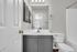 Bright, modern bathroom featuring sleek gray cabinetry, a large mirror, and classic white fixtures.