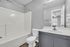 Elegant bathroom featuring a sleek gray vanity, pristine white fixtures, and ample natural light streaming through the doorway.