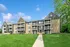 Charming apartment building with modern balconies, situated in a lush green setting under a bright blue sky.
