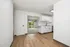 Bright apartment interior with elegant wooden flooring, modern white kitchen cabinets, and a spacious living area with a large window offering lush, green views.