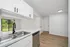 Modern kitchen with sleek white cabinetry, stainless steel sink, and a scenic view of lush greenery through a large sliding glass door.