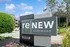 Charming apartment community sign at reNEW Kentwood, surrounded by lush greenery and vibrant flowers, with modern buildings in the background.