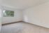 Bright and airy room with plush carpeting and a large window offering tranquil greenery views.