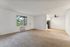 Bright and airy apartment living space with plush carpet, large window, modern ceiling fan, and sleek kitchen area.