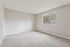 Bright and airy bedroom with plush carpet, large window, and neutral walls, offering a serene view of lush greenery.