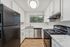 Modern kitchen featuring sleek black appliances, white cabinetry, and marble countertops with a window view.