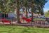 Charming outdoor playground area with vibrant red play equipment, nestled under lush pine trees, offering a serene and fun environment for children.