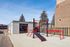 Inviting outdoor exercise area with modern red and black fitness equipment, surrounded by a fresh urban landscape and bright blue sky.