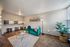 Chic living area featuring a plush green sofa, elegant floor lamp, and a cozy breakfast bar with stools. Natural light floods the space, highlighting the modern decor and vibrant houseplant.