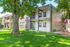 Charming apartment exterior with lush green lawn, mature trees, and inviting balconies nestled in a tranquil setting.