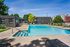 Inviting apartment complex featuring a refreshing outdoor swimming pool, surrounded by lush greenery and spacious lounging areas under a clear blue sky.