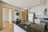 Modern kitchen with sleek black countertops, integrated stainless steel appliances, and in-unit washer and dryer. Abundant natural light enhances the open feel.