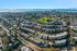 Scenic aerial view of a vibrant neighborhood featuring modern apartment complexes, lush green parks, and a stunning waterfront backdrop.