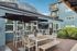 Charming outdoor patio at Arrive Magnolia with modern tables, chairs, and ample shade from large umbrellas, set against an elegant blue building.
