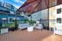 Chic modern terrace with comfortable gray seating, wooden decking, and elegant overhead shade, surrounded by colorful apartment buildings and lush greenery.