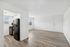 Bright open-concept living area with sleek flooring, adjacent to a modern kitchen featuring a stylish black refrigerator.