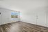Bright and inviting empty room featuring sleek wood flooring, expansive white walls, and a large window overlooking a tranquil outdoor scene.