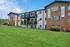 Charming renovated apartment building with balconies, lush green lawn, and prominent 'Now Leasing' banners.