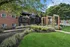 Charming leasing office entrance of a brick apartment complex with vibrant landscaped gardens and inviting greenery under a clear blue sky.