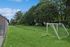 Inviting green outdoor space featuring a soccer field with two goalposts, bordered by lush trees.