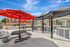 Charming outdoor patio with red umbrellas, modern picnic tables, and built-in grills set against a sunny backdrop.