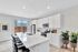 Modern kitchen with sleek white cabinetry, a spacious island, and stainless steel appliances. Bright and airy atmosphere with sliding glass doors and stylish bar seating.