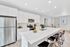 Modern kitchen with sleek stainless steel appliances, elegant white cabinetry, and a spacious quartz island with seating in a bright, open-concept design.