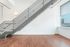 Modern apartment interior with sleek metal staircase, elegant hardwood flooring, and plentiful natural light from large window showcasing urban views.