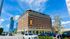 Charming historic brick building with modern penthouse views, located in a bustling city setting under a vibrant blue sky.