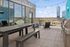 Chic rooftop patio with string lights, large dining table, cozy seating, and BBQ grills, offering stunning cityscape views.
