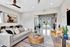 Modern living area with a stylish gray sofa, chic wooden coffee table, vibrant artwork, and abundant natural light accenting the spaciousness.