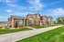 Charming townhouses with modern brown siding, lush green lawns, and inviting entryways under a clear blue sky.