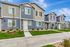 Charming modern townhouses with sleek gray siding, well-manicured lawns, and inviting entrance paths, set against a vibrant blue sky backdrop.