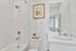 Elegant bathroom with modern fixtures, featuring a chic framed floral artwork, luxurious bathtub, and pristine white vanity.