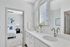 Bright, modern bathroom with dual sinks, elegant fixtures, and a glimpse into a cozy, well-decorated bedroom.