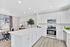 Spacious modern kitchen with sleek white cabinetry, large island, and stainless steel appliances connected to a cozy living area with elegant decor.