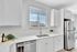 Bright and modern kitchen with sleek white cabinetry, stainless steel appliances, and a large window allowing natural light to fill the space.