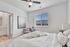 Bright and inviting bedroom with modern decor, featuring a cozy armchair, stylish artwork, and abundant natural light through large windows.