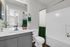 Chic bathroom with modern gray vanity, elegant white countertop, and luxury toiletries. Green and white shower curtain adds a stylish touch.