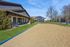 Inviting community space featuring a sand volleyball court, modern clubhouse with blue benches, and well-maintained greenery under a clear blue sky.