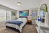 Bright and inviting bedroom featuring a soft carpet, modern art pieces, and an elegant blue bed. Large windows and chic decor enhance the serene ambiance.